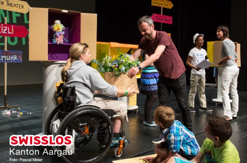 Rollstuhlfahrerin erhält Blumen. Femme en fauteuil roulant recevant des fleurs. Donna in sedia a rotelle riceve dei fiori.