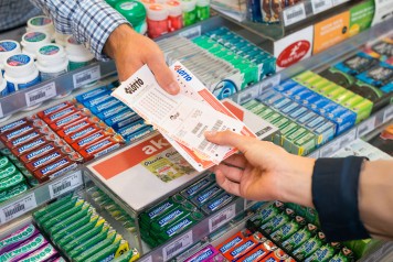 Gros plan sur le vendeur remettant au client son bulletin Swiss Lotto et son reçu.